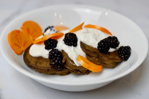 white plate with pancakes on top topped with cream, blackberries, and fruit