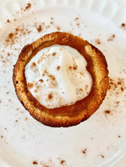 mini pumpkin pie topped with whipped cream and cinnamon on a white plate