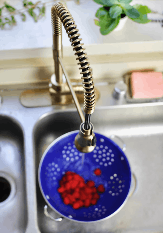 A kitchen faucet with a blue colander and berries