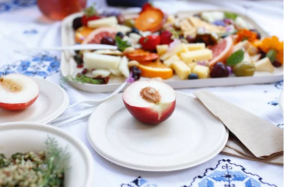 A halved peach on a plate surrounded by more fruits and cheeses