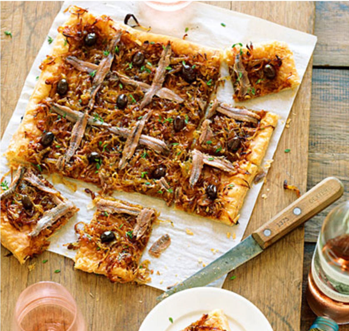 Pissaladière sliced into squares with a knife next to it