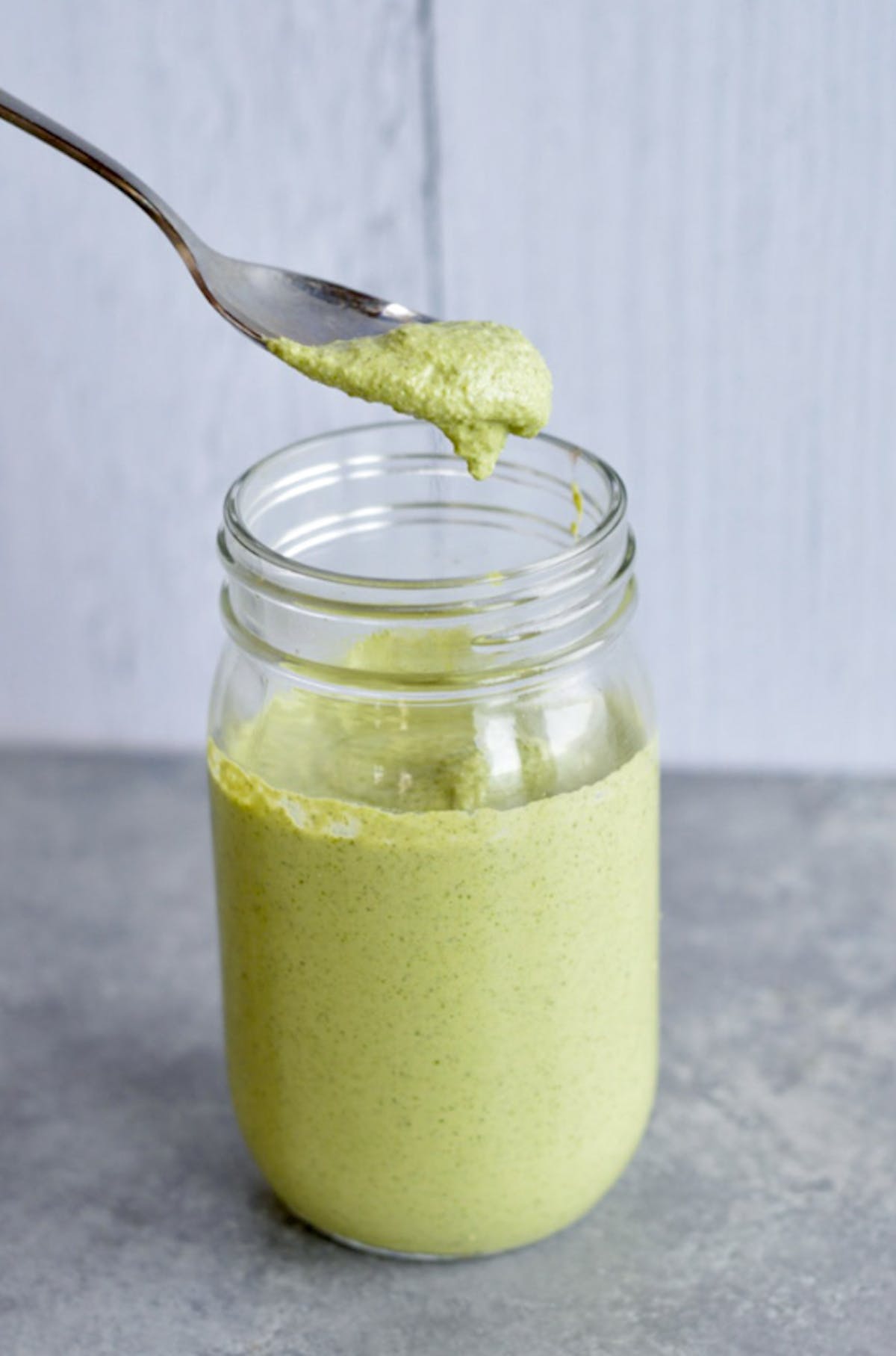 a spoon dipping into a glass mason jar filled with green dressing