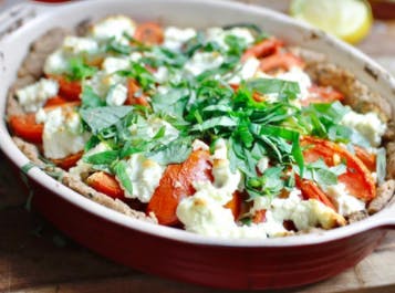 A tomato tart in a red oval dish with cheese and basil
