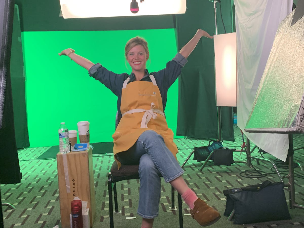 Chef Anja with hands raised smiling in front of a green screen