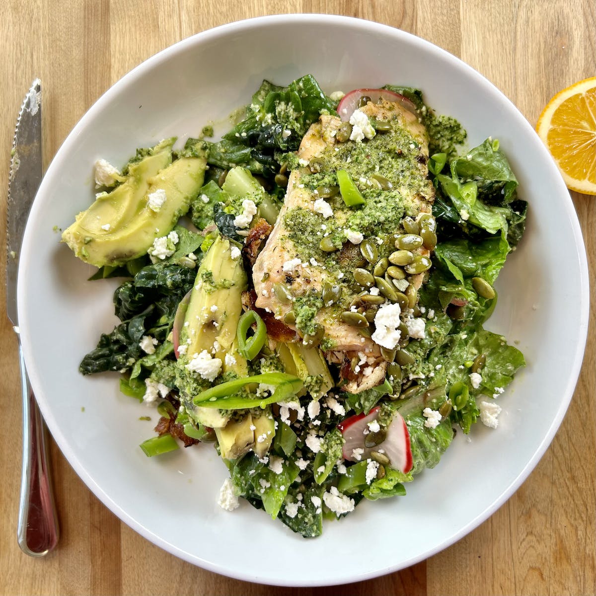 white bowl filled with greens, salmon, avocado, and a green sauce