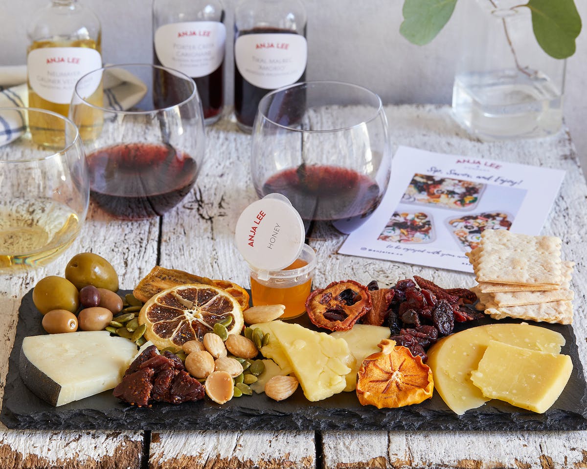 a small platter of cheese and fruits with glasses of red wine