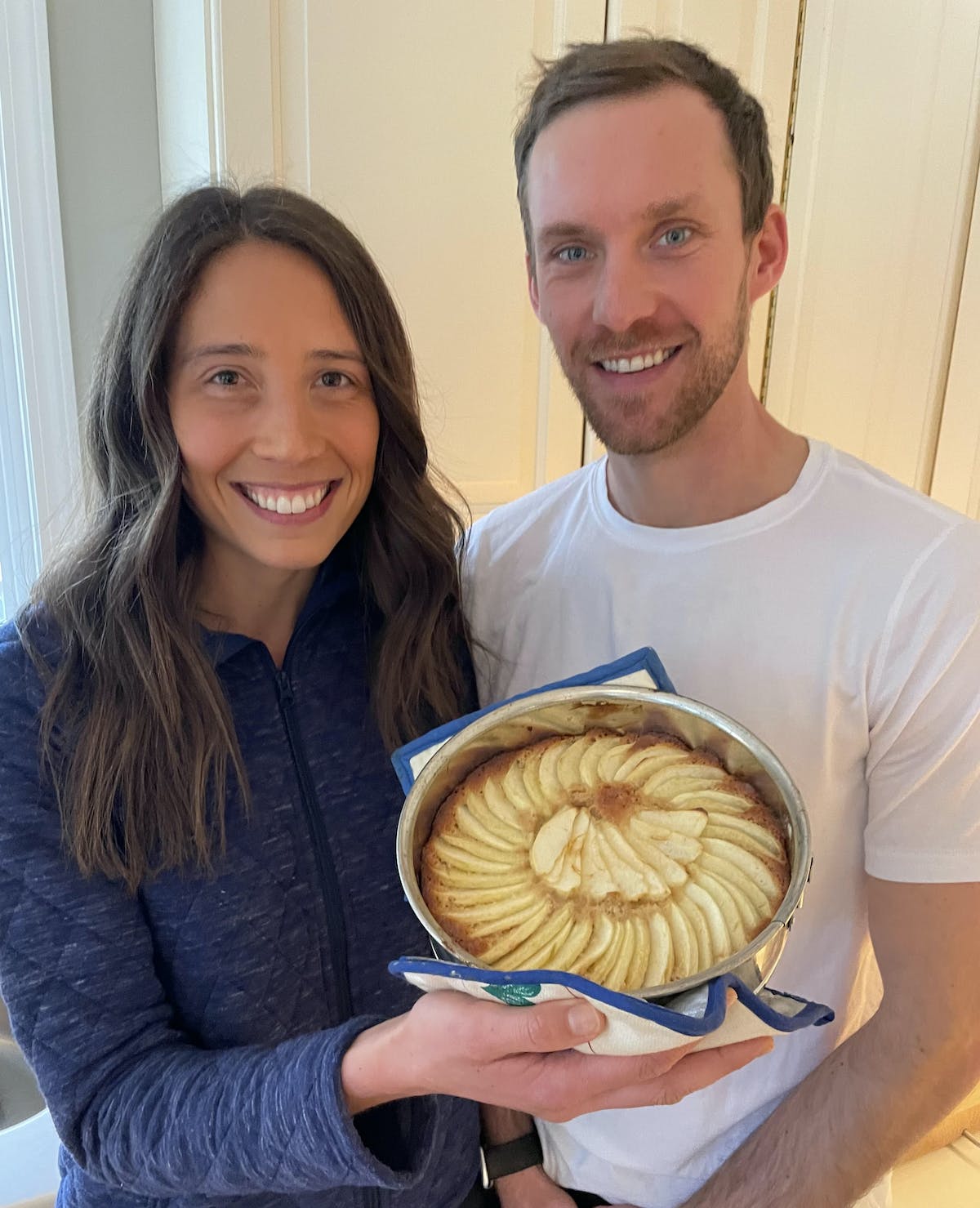 a man and woman smiling holding up an apple galette