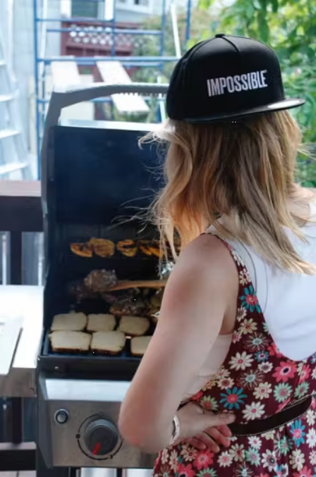 woman grilling with a black backwards hat that says impossible on it