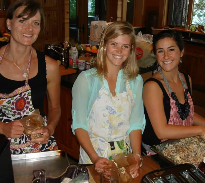 3 women smiling and cooking together in aprons